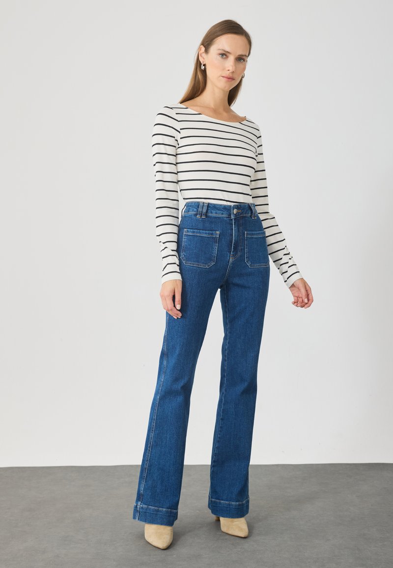 Gestreepte lange mouwen top in wit en zwart, gecombineerd met hooggetailleerde blauwe denim flared pants met achterzakken en omgeslagen zomen.