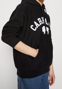 Černá mikina s kapucí z bavlněné směsi, s kapsou vpředu, žebrovanými manžetami a bílým nápisem "CARHARTT" s grafikou bizona.