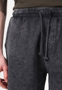 Sivé joggingové nohavice vyrobené z jemnej látky s elastickým pásom a šnúrkou na stiahnutie. Majú štruktúrovaný povrch a voľný strih.