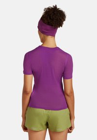 Top corto a maniche corte viola in rete con un design aderente, abbinato a pantaloni corti verdi con dettagli riflettenti. Tessuto morbido e materiale leggero.