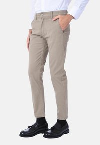 Chino di colore neutro realizzati in tessuto morbido, con vestibilità slim, chiusura con bottone frontale e tasche laterali. Abbinati a mocassini neri.