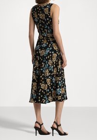 Svart blommig klänning med gula och blå mönster, ärmlös design, flödande tyg, knälång nederdel, matchad med svarta högklackade sandaler.