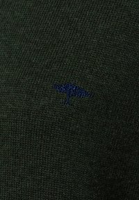 Dunkelgrüner Strickpullover mit einem kleinen blauen gestickten Logo eines Vogels auf der Vorderseite. Der Stoff sieht weich aus und hat eine glatte Textur.