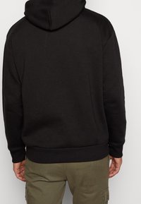 Sudadera negra con un diseño sencillo, que incluye una capucha con cordón y puños acanalados. La tela parece suave, con una textura mate.