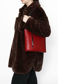 Rode leren handtas met een gestructureerd, gestippeld patroon en een zwarte rits, gedragen over een bruine nepbontjas.