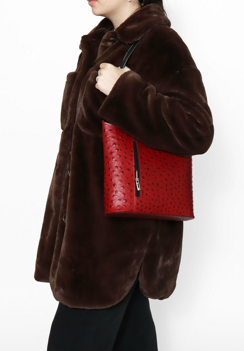 Rode leren handtas met een gestructureerd, gestippeld patroon en een zwarte rits, gedragen over een bruine nepbontjas.
