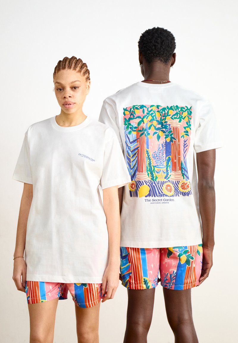 Witte T-shirt met een kleurrijke grafische print op de achterkant, met kolommen en loof. Gecombineerd met gestreepte shorts in roze en blauw.
