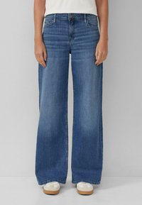 Jeansy z szerokimi nogawkami w średnim niebieskim odcieniu. Posiadają klasyczny fason z pięcioma kieszeniami i zapięcie na guzik. Miękka faktura z delikatnym spraniem.