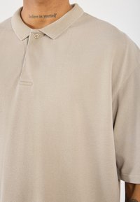 Beige polo t-shirt van textiel met een structuur, met een kraag en een enkele knoopsluiting. Korte mouwen en een relaxte pasvorm.
