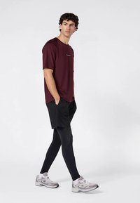 Bordowa koszulka z krótkim rękawem z małym logo, w połączeniu z czarnymi sportowymi szortami i czarnymi legginsami. Szare buty do biegania dopełniają stylizację.