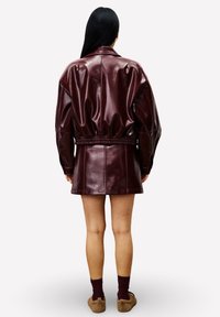 Bordeaux faux leren jack met een getailleerde taille, oversized mouwen en een rugdetail, afgewerkt met een gladde, glanzende textuur.