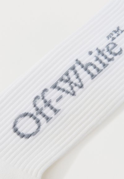 Tissu blanc côtelé avec le texte « Off-White™ » tricoté en gris en diagonale sur la surface.