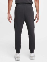 Svarta joggingbyxor för män i mjukt tyg, med elastisk midja, sidofickor med lock, avsmalnande ben och muddade benslut. Sneakers med gummisula syns.