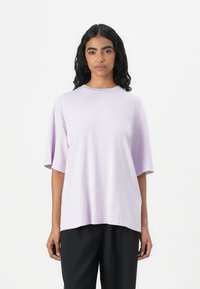 Tricou oversized de culoare liliac, fabricat din bumbac moale, având gât rotund și umeri căzuți. Purtați-l împreună cu pantaloni negri, lejerați.