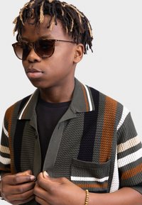 Knit shirt jacket in green, brown, and black stripes, with a chest pocket and a collared neckline; layered over a black shirt.