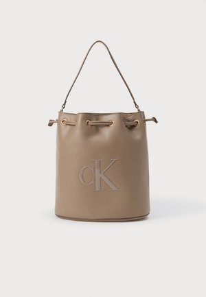 Beige faux læder spandtaske med rund bund, snoromhugning i toppen og en enkelt skulderrem. Prægede "CK" logo på forsiden.