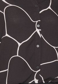 Blouse noire avec un motif abstrait blanc, dotée d'une fermeture par boutons sur le devant et de boutons ronds noirs. Tissu doux avec une texture lisse.