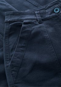 Tummansinisiä housuja, jotka on valmistettu kudotusta kankaasta. Housuissa on nappikiinnitys, laskostettu etuosa ja tarkat ompeluyksityiskohdat. Pintakuvio on sileä.