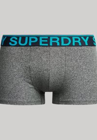 Bañadores grises hechos de un tejido texturizado con una cintura elástica negra y turquesa que presenta el logo "SUPERDRY" de forma prominente.