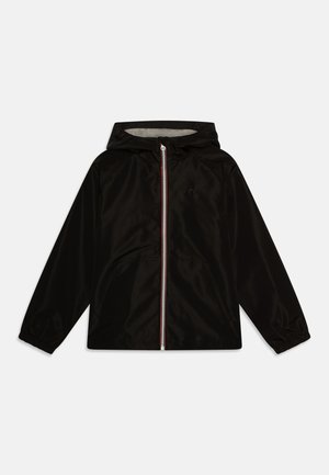 Chaqueta negra con capucha de textura suave, cierre de cremallera con una franjas rojas y blancas, y puños elásticos. Incluye bolsillos laterales.