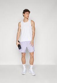 Witte sporttanktop, lavendel sportshorts, witte sneakers en een zwarte waterfles. Bevat het Nike-logo op de tank en de shorts. Soepele stoftextuur.