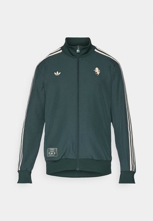 Grøn zip-up jakke med høj krave, tre hvide striber på ærmerne, logo patches, ribbede manchetter og talje, lavet af et blødt stof.