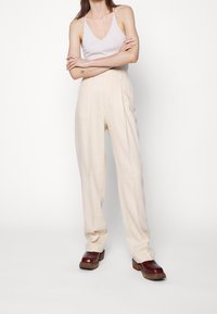 Krämfärgade skräddarsydda byxor med en lös passform, med framfickor och slät textur, i kombination med mörkbruna platåskor.