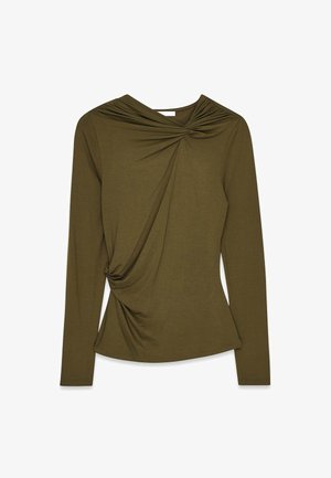 Ilgas rankovės marškinėliai alyvuogių spalvos, su suktais detalėmis priekyje ir minkšta tekstūra. Prigludusi forma su apvaliu apvadu ir surinkta kaklo linija.