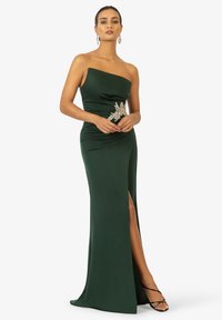Abito verde smeraldo senza spalline con silhouette aderente, dettagli arricciati sul lato, alta spacco laterale e decorazioni argentate in vita.