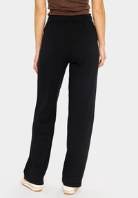 Juodieji laisvi treningai su elastine juosta, sklandžia tekstūra, tiesaus modelio ir su užlenktais apačiais.