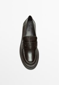 Black leather loafers with a smooth, glossy finish, featuring a decorative strap across the vamp and a rounded toe. Subtle stitching detail.
