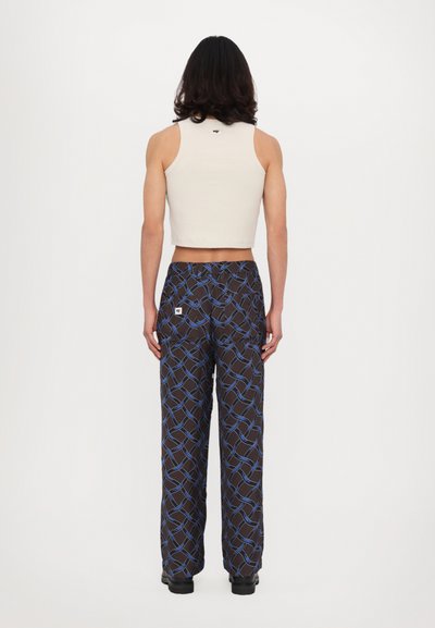 Débardeur beige court associé à un pantalon large noir à motif avec un design géométrique bleu et des poches latérales.