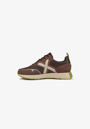 Zapatilla de malla marrón con acentos beige, suela de goma y detalles en verde. Presenta un diseño aerodinámico y una textura perforada para mayor transpirabilidad.