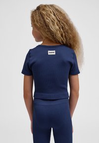 Mørkeblå ribbet atletisk top med korte ærmer og cropped design, der har et rektangulært logo-patch på den øverste ryg.