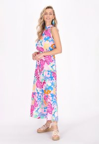 Rochie maxi florală cu fundal roz, cu frunze albastre, portocalii și verzi. Material ușor, fără mâneci, cu o talie strânsă.