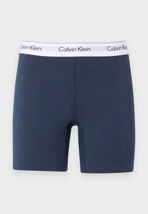 Marineblaue Boxershorts mit weißem elastischem Bund, der mit wiederholtem schwarzem Calvin Klein Logo versehen ist, flach auf hellem Hintergrund dargestellt.