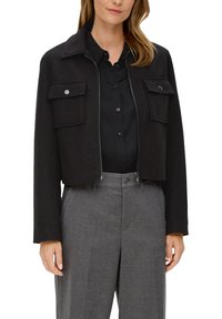 Czarna, krótka kurtka z kołnierzem, zamkiem błyskawicznym z przodu i dwiema kieszeniami na piersi. Wykonana z teksturowanej tkaniny, zestawiona z szarymi spodniami z wysokim stanem.