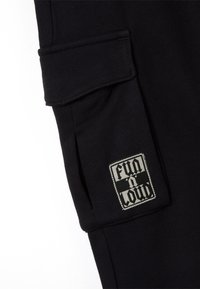 Zwarte katoenen joggingbroek met een zijzak en een rechthoekig label waarop "FUN A LOUD" staat in contrasterende witte en zwarte letters.