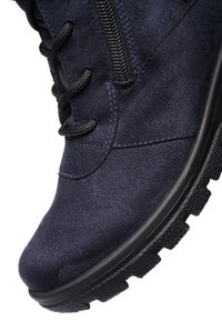 Close-up af en navy ruskindsstøvle med sorte snørebånd, sidelås og tekstureret gummisål.