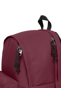 Bordová batoh vyrobený z hladkého, odolného materiálu, s zaoblenou horní částí a černými kovovými detaily, které mají stahovací uzávěry.