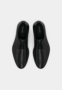 Μαύρα δερμάτινα παπούτσια με λείο φινίρισμα, σχέδιο με κορδόνια και στρογγυλές μύτες. Το εσωτερικό διαθέτει επώνυμο πέλμα. Μινιμαλιστικά και κομψά.