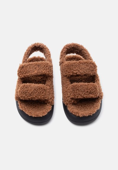 Καφέ χνουδωτά σανδάλια με δύο ρυθμιζόμενους ιμάντες και ανοιχτές μύτες, με μαύρες καουτσούκ σόλες για καθημερινή χρήση.