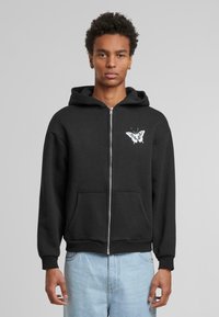 Sort zip-up hoodie i blandet bomuld med en frontlomme og et neutralt sommerfuglegrafik på brystet. Fôret hætte med justerbare snore.