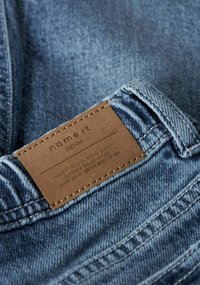 Jeans in denim di colore azzurro chiaro con una toppa in pelle con la scritta "name it", decorati con cuciture lungo le cuciture e la cintura.