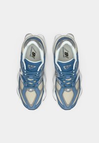 Pair of blue and beige New Balance 9060 running shoes viewed from above on a white background.