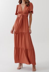 Rostfärgad maxiklänning i lätt tyg, med korta puffärmar, djup V-hals, knytmidja och flerlagrad volangnederdel.
