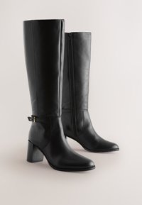 Bottes noires en cuir montant jusqu'aux genoux avec un bout pointu, un talon bloc et une fermeture éclair latérale. Dotées d'une bride décorative avec un accent doré.