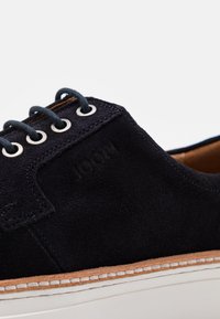 Sneaker nera in camoscio con tomaia testurizzata, suola in gomma bianca e occhielli rotondi in argento per i lacci. Nome del marchio impresso sul lato.