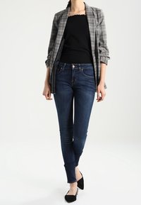 Blazer de cuadros gris sobre una blusa negra, combinado con jeans ajustados azul oscuro y bailarinas negras. El blazer tiene mangas arremangadas y un diseño entallado.