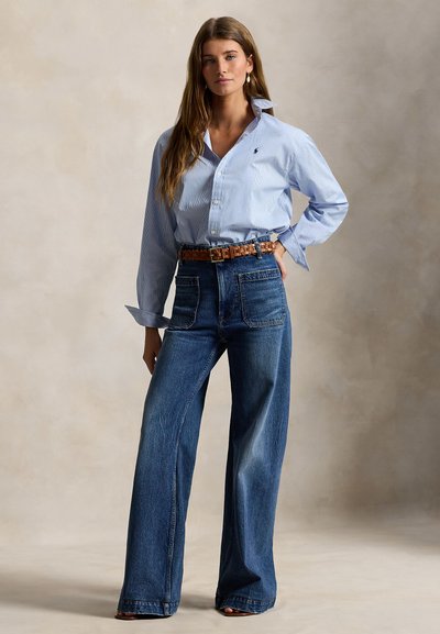 Ανοιχτό μπλε πουκάμισο με ρίγες και κουμπιά, μακριά μανίκια, συνδυασμένο με τζιν παντελόνι σε σκούρο μπλε με φαρδιά πατ, και ταμπά πλεκτή ζώνη. Ομαλές υφές απαλού, casual υφάσματος.